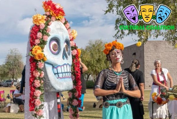 Woman in Day of the Dead attire with a large decorated skull figure outdoors.