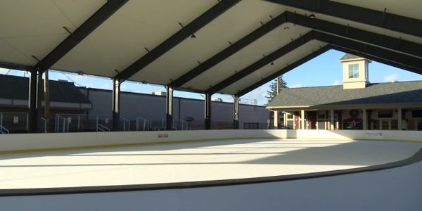 Covered outdoor ice skating rink with bright sunlight and clear blue sky.