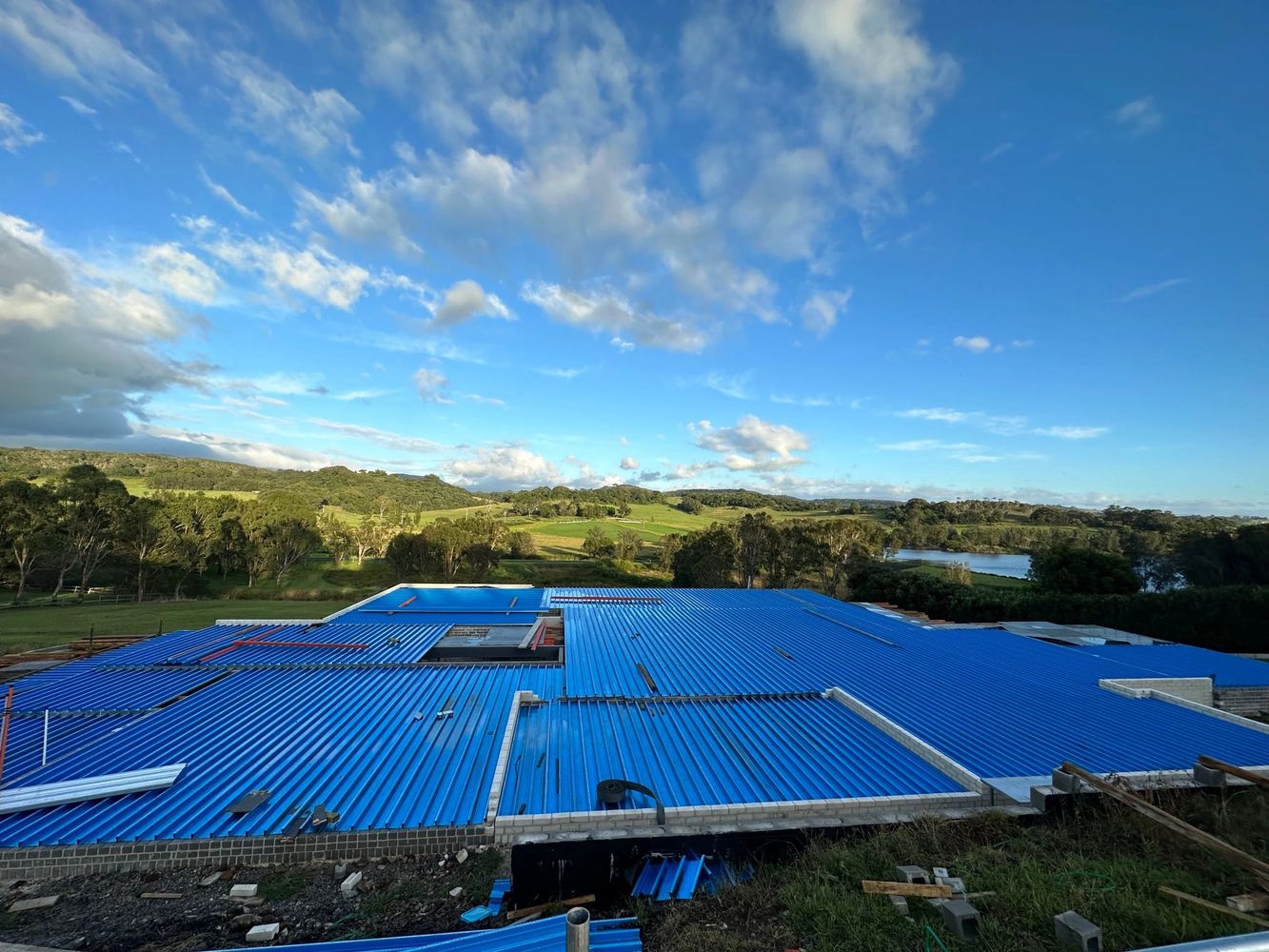 A large blue corrugated metal roof under a clear sky with green landscape.