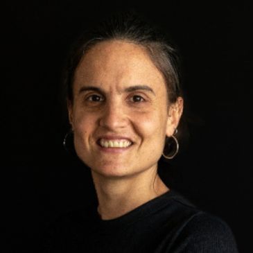 Portrait of a smiling woman with hoop earrings against a black background.
