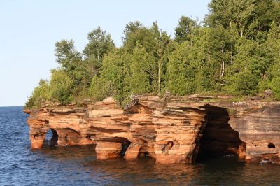 Rocky cliffs with natural arches along a forested shoreline.