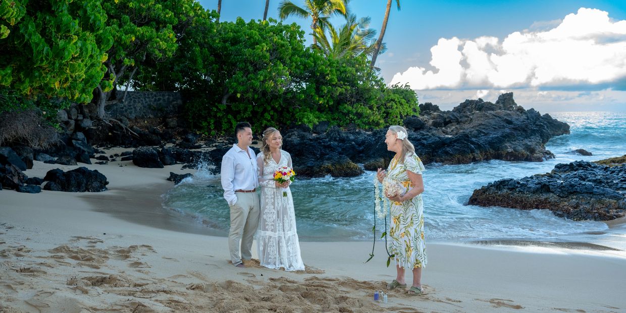 Couple having a beach wedding ceremony with an officiant by the ocean and rocks.