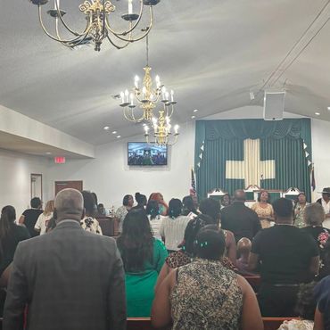 Congregation gathered inside a church with chandeliers and a cross.