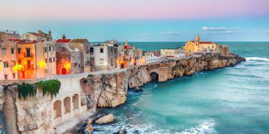 Coastal town with colorful buildings along rocky cliffs at sunset.