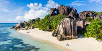 Pristine beach with unique granite boulders and clear blue water under a bright sky.