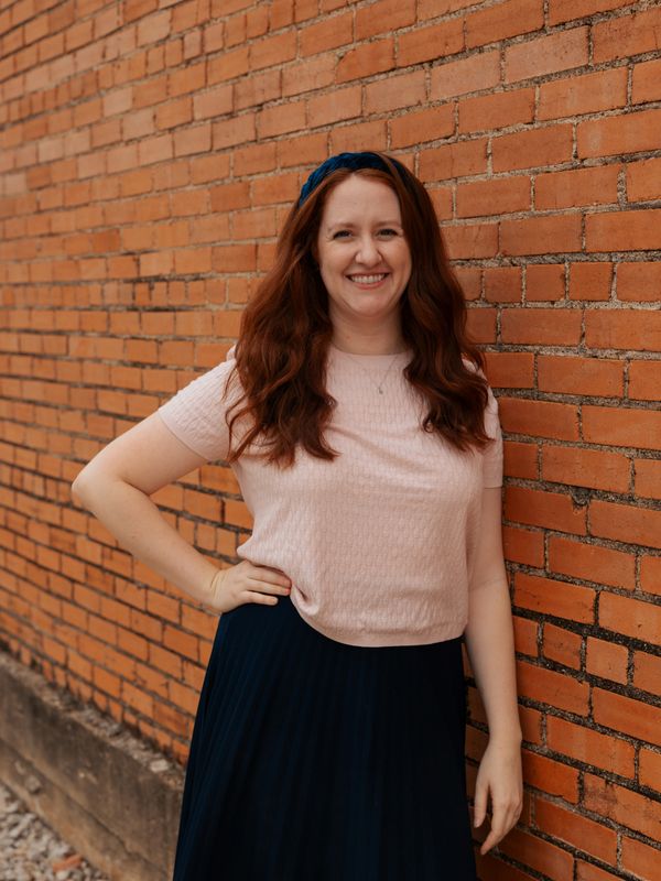 A woman with long red hair smiles beside a brick wall.