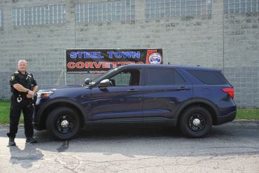 Police officer standing next to a police SUV outside a building.