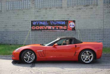 Red Corvette convertible parked in front of a Steel Town Corvettes sign.