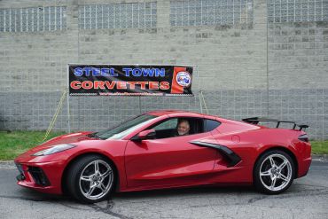 Red Corvette sports car parked by a Steel Town Corvettes banner.