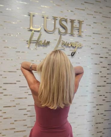 Woman with long blonde hair in front of Lush Hair Lounge sign.