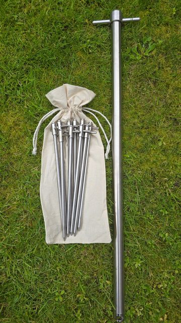 A set of metal stakes and a long metal pole on grass with a drawstring bag.