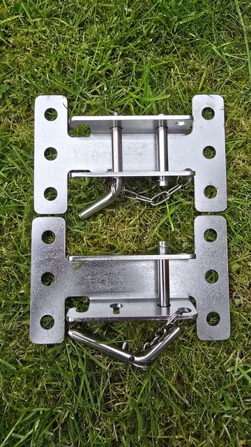 Two metal bracket fixtures with pins and chains lying on grass.