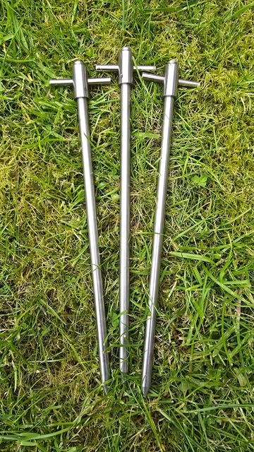 Three metal ground stakes lying on green grass.