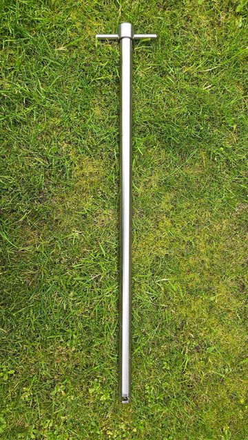 A long metal rod with a T-handle lying on grass.