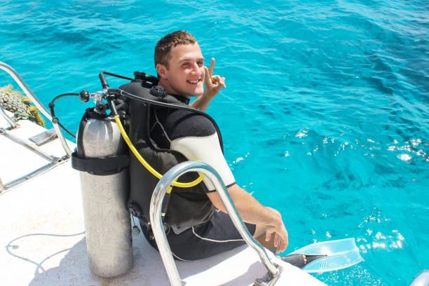 A happy scuba diver on a boat preparing to dive into clear blue water.