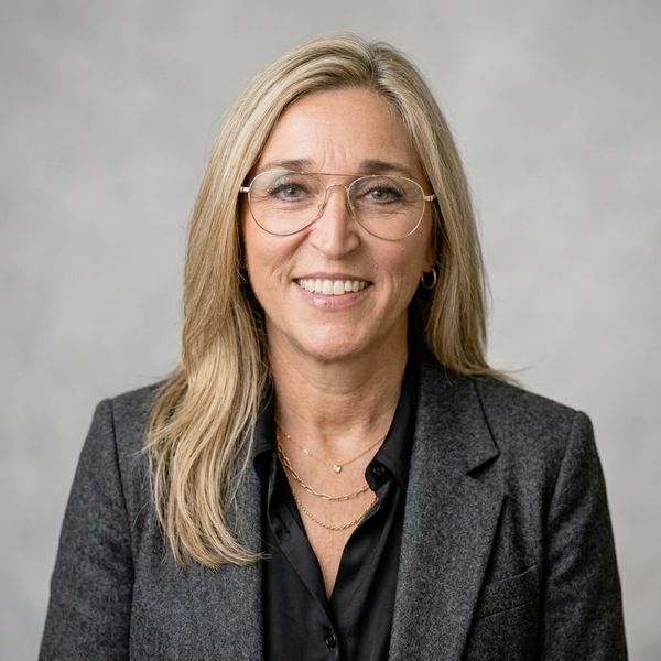 Smiling woman with blonde hair wearing glasses and a gray blazer.