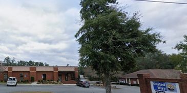 A tree in front of a brick building with cars and a United Way sign.