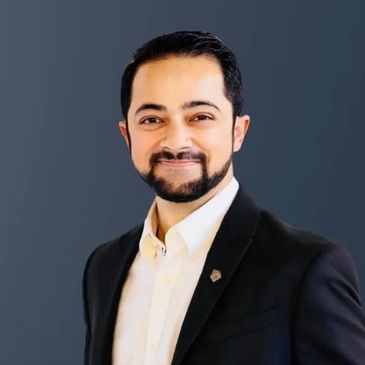 Professional man in a suit smiling against a dark background.