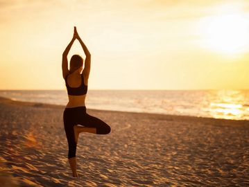 Person practicing yoga on the beach at sunset.