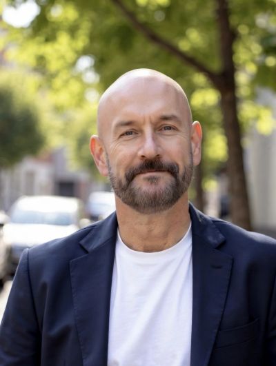 Smiling bald man with beard wearing a blazer and white t-shirt.