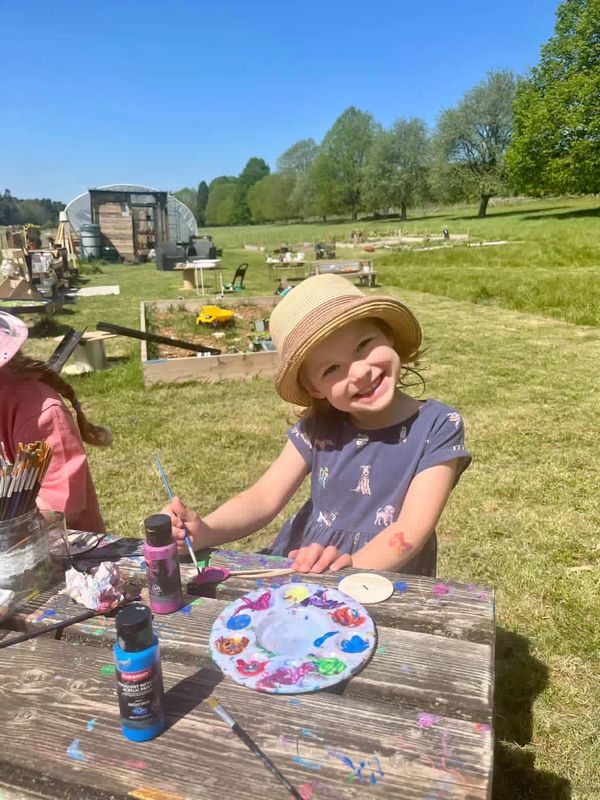 A smiling child painting outdoors on a sunny day.
