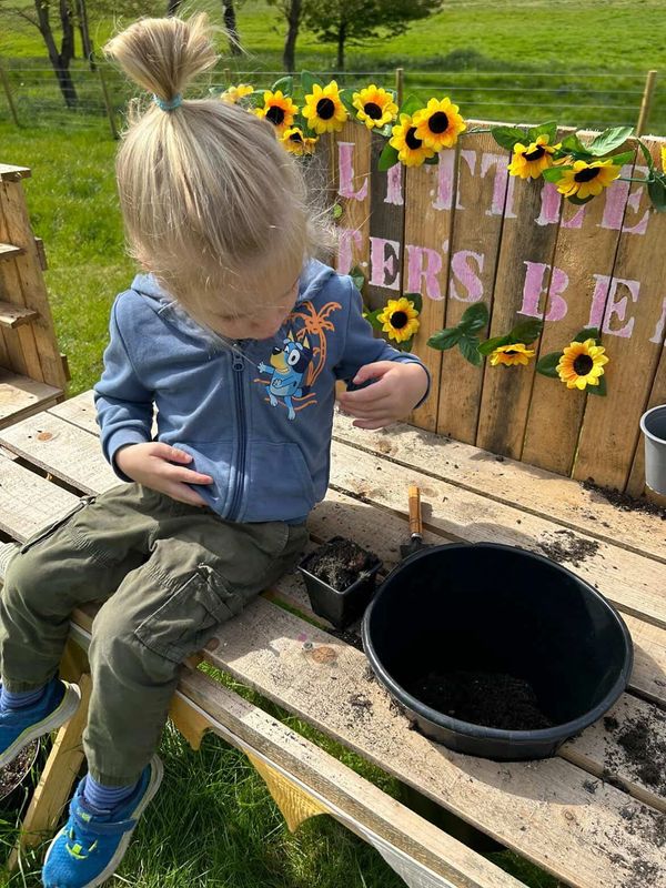Child sitting on a wooden bench, gardening with soil and pots.