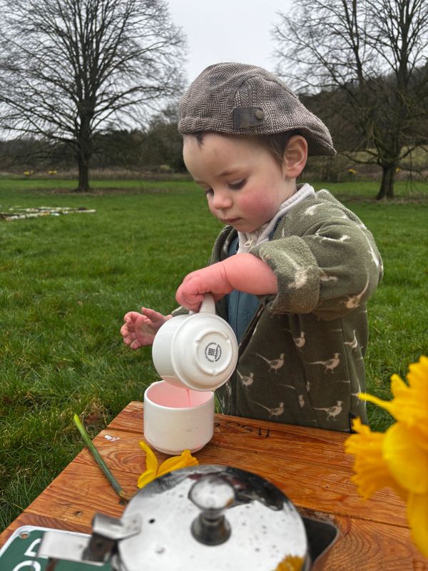 A child in a cap pouring pink liquid into a cup outdoors.