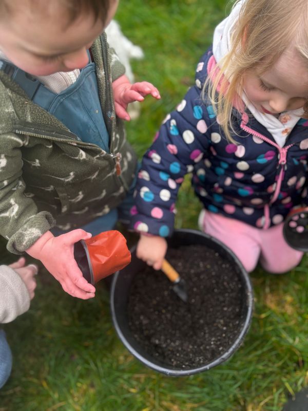 Two children playing with soil and gardening tools outdoors.