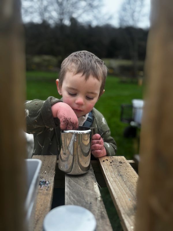Young boy playing with dirt and a metal cup outdoors.