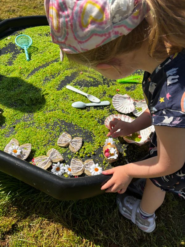 A child plays with toy sea creatures and shells in a water table outdoors.