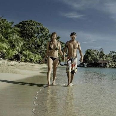 A couple walks hand in hand along a tropical beach shore.