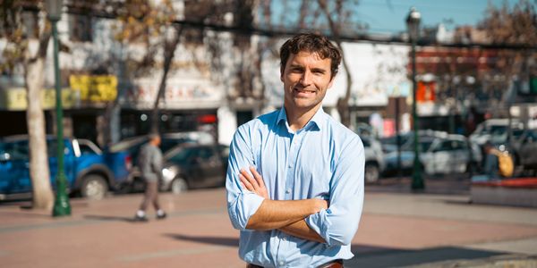 Smiling man in a light blue shirt standing outdoors with arms crossed.