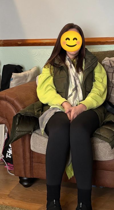 Person sitting on a couch wearing a green vest and yellow sweatshirt.