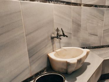 A marble hand-shaped sink with a vintage faucet in a tiled room.