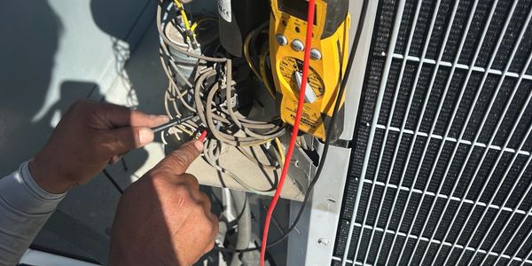Commercial HVAC technician testing electrical components on a rooftop condenser unit.