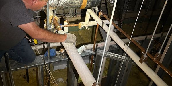 Commercial facility maintenance technician performing overhead plumbing and HVAC pipe repair.