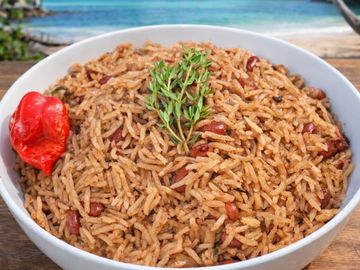 Bowl of seasoned rice and beans garnished with a pepper and thyme.