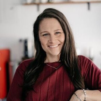 Smiling woman with long brown hair in a cozy indoor setting.