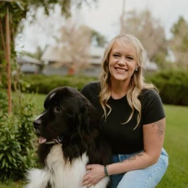 Woman kneeling beside a large black and white dog outdoors.