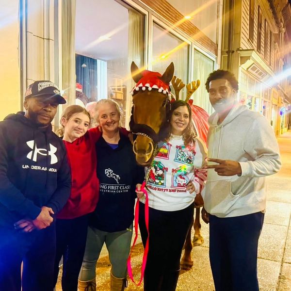 Group of five people posing with a horse on a city sidewalk at night.