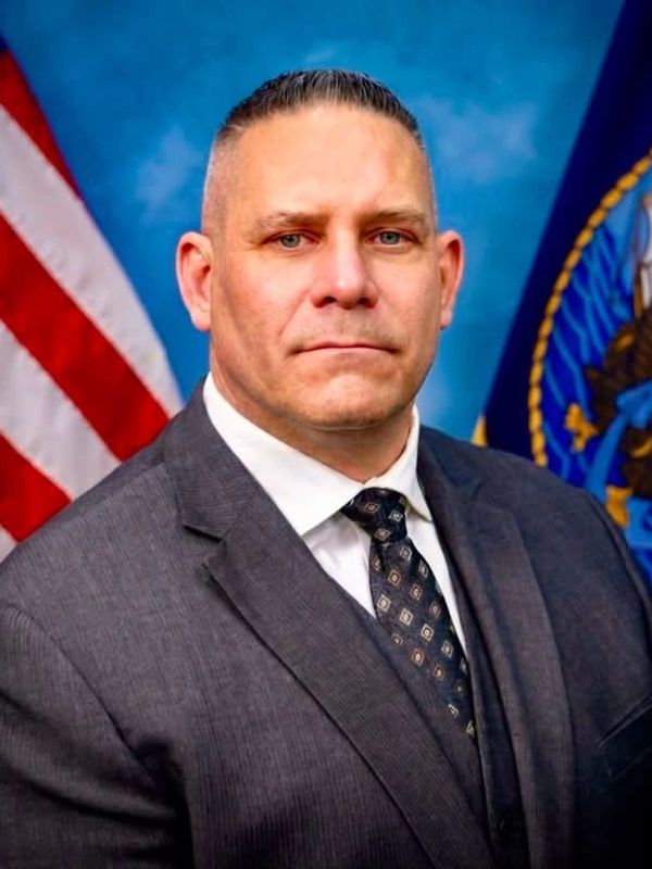 Man in a suit with patriotic flags in the background.