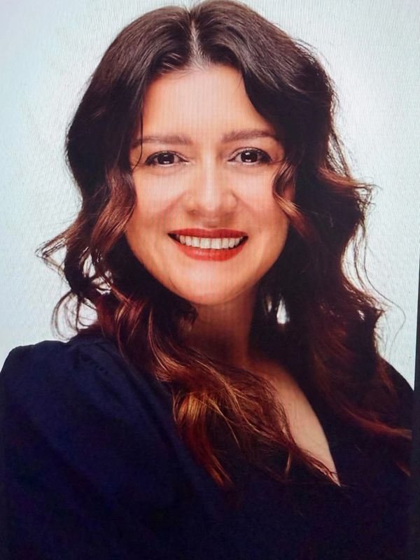 Smiling woman with wavy brown hair in dark clothing.