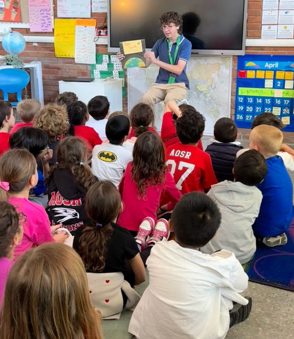 Student reading a book to a group of children in a classroom.