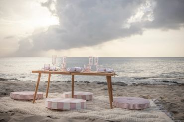 Beachside low table setup with cushions and tableware at sunset.