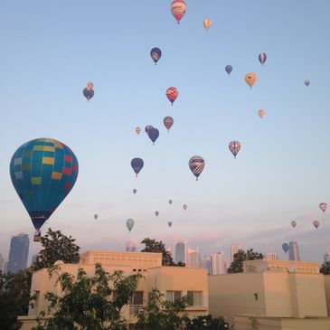 Many hot air balloons flying over Dubai during sunrise.