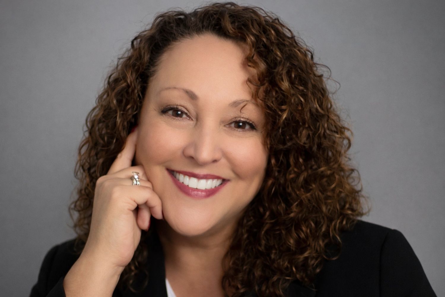 Smiling woman with curly hair and a ring on her finger.