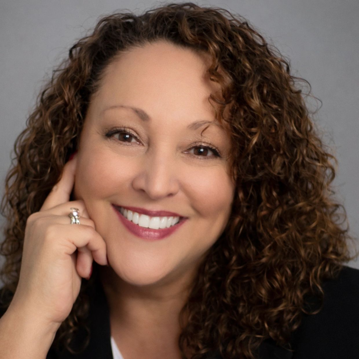 Smiling woman with curly hair and a ring on her finger.