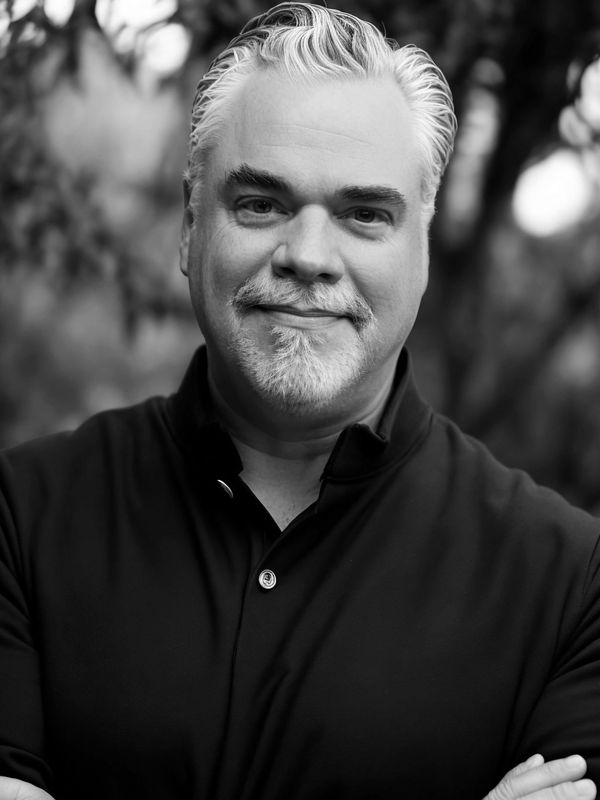 Black and white portrait of a smiling middle-aged man with crossed arms.