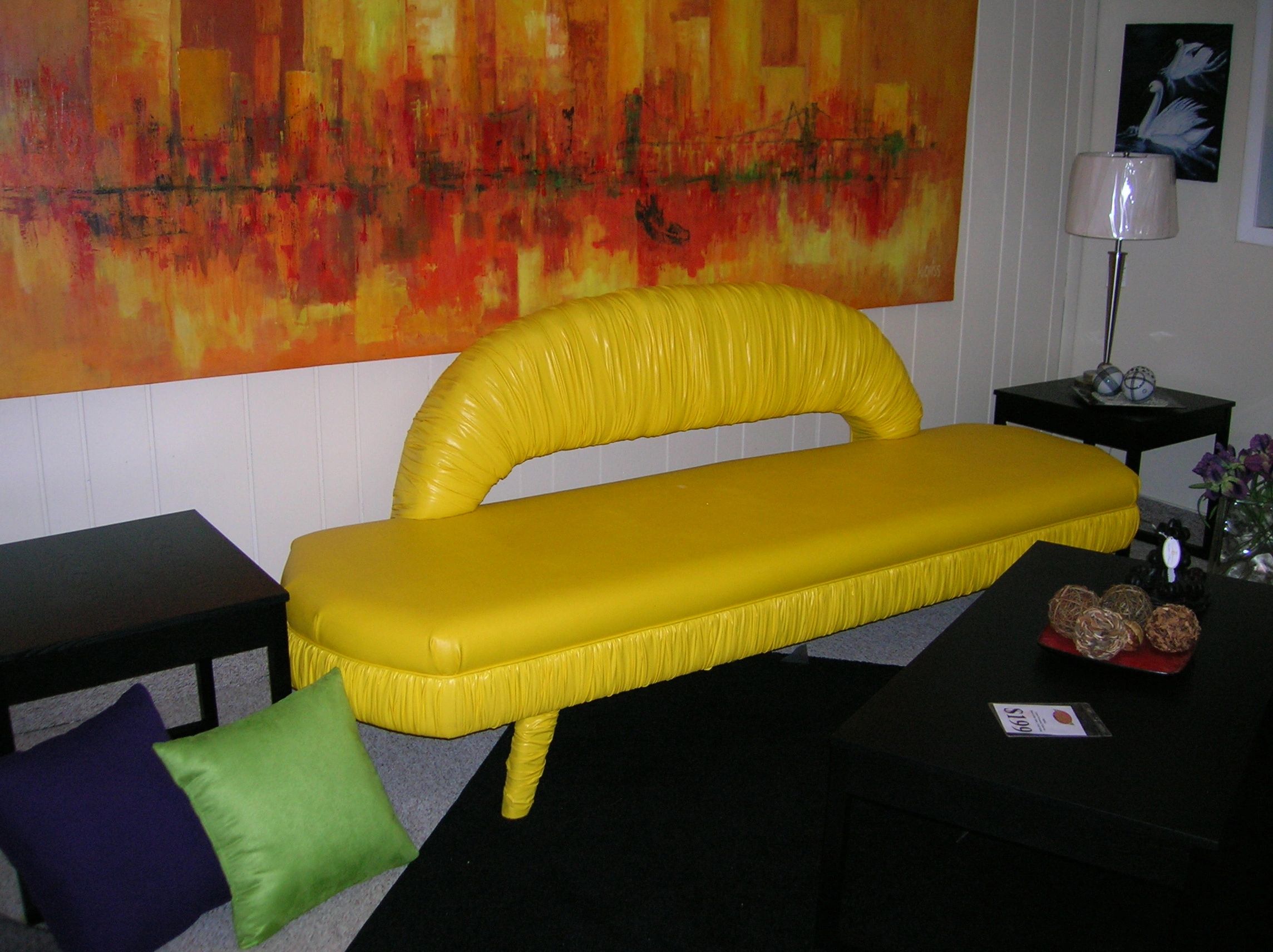 Bright yellow vintage couch with colorful cushions and a vibrant abstract painting in a cozy living room.