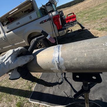 A gloved hand holding a welded metal pipe outdoors near a truck.